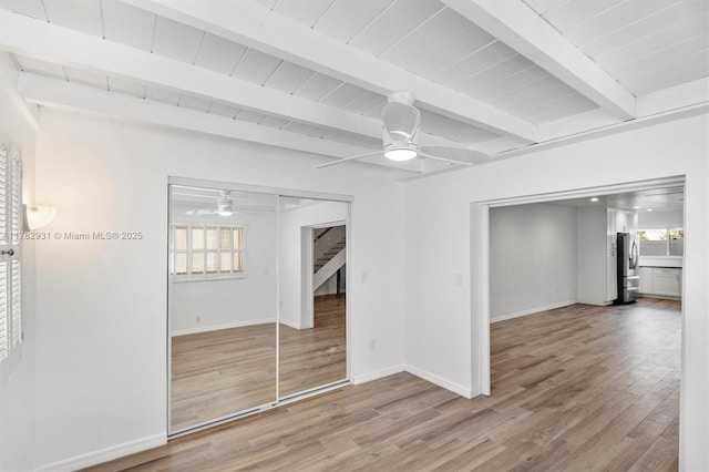 interior space with baseboards, freestanding refrigerator, beam ceiling, ceiling fan, and wood finished floors