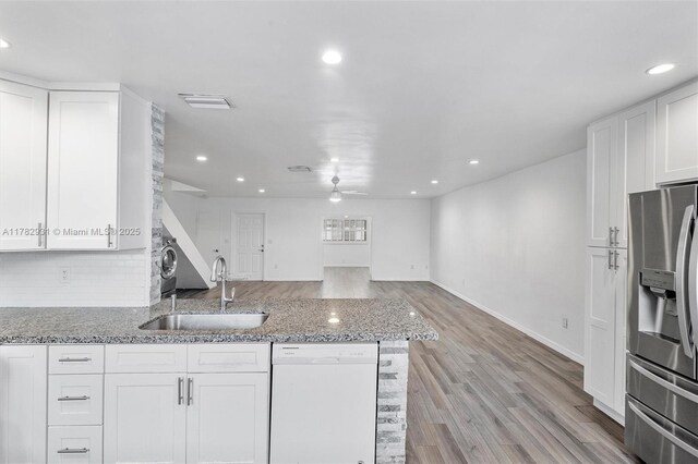 kitchen with light stone countertops, white cabinetry, stainless steel refrigerator with ice dispenser, dishwasher, and a sink