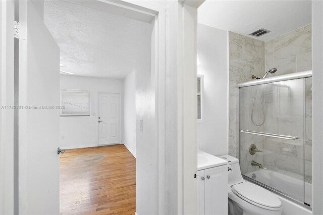 bathroom with visible vents, bath / shower combo with glass door, toilet, vanity, and wood finished floors