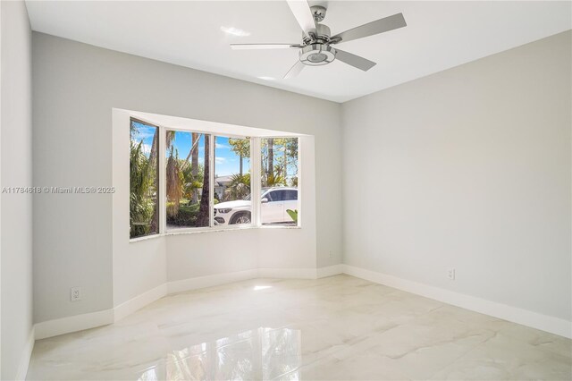 spare room with marble finish floor, baseboards, and ceiling fan