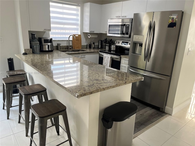 kitchen featuring stainless steel appliances, a peninsula, a breakfast bar area, a sink, and light tile patterned floors