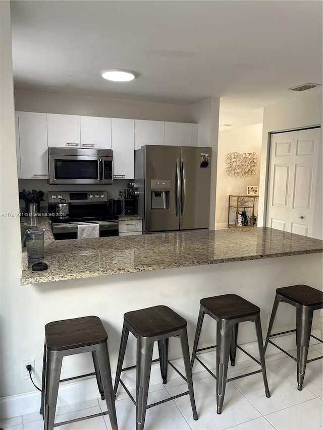 kitchen with dark stone counters, a breakfast bar area, a peninsula, appliances with stainless steel finishes, and visible vents