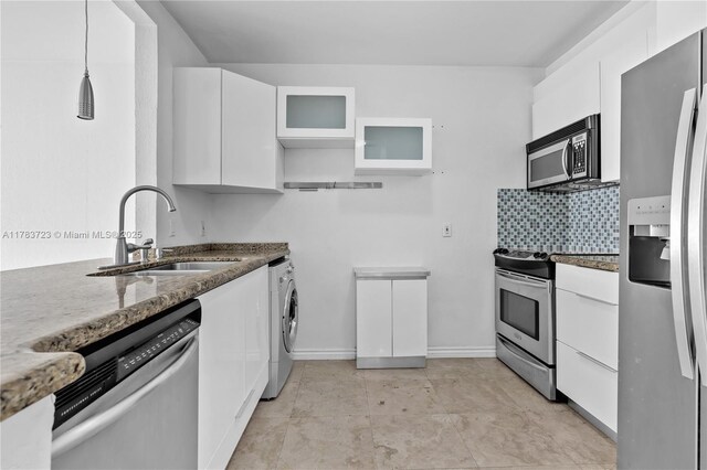677 NE 24th St Unit 504, Miami, FL 33137 - kitchen with stainless steel appliances, washer / dryer, dark stone countertops, white cabinetry, and glass insert cabinets