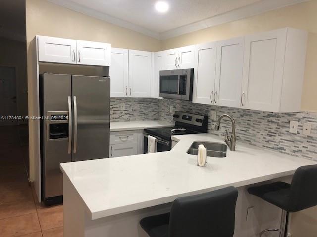 kitchen with tasteful backsplash, a sink, light countertops, a peninsula, and stainless steel appliances