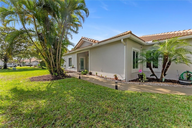 view of side of property featuring a yard, a tile roof, and stucco siding
