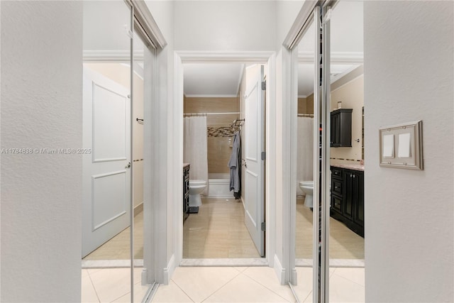 hall with a textured wall, ornamental molding, and light tile patterned floors