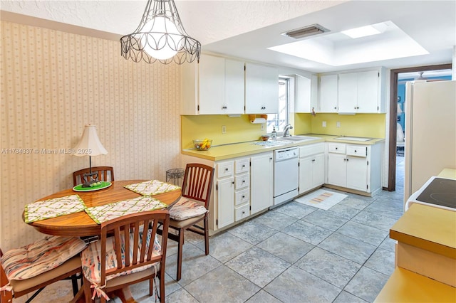 kitchen with white cabinets, light countertops, a raised ceiling, a sink, and white appliances