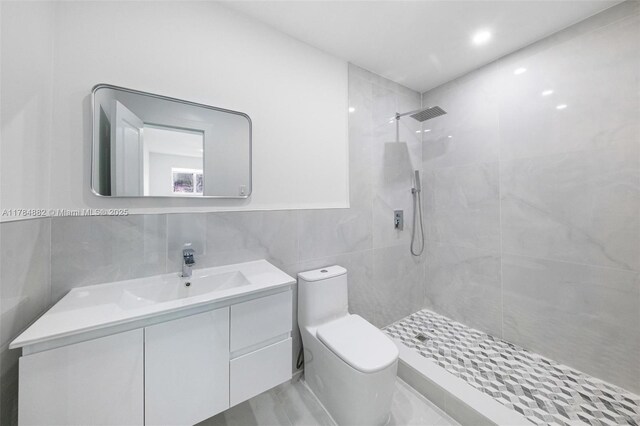 bathroom featuring vanity, tile walls, a tile shower, and toilet