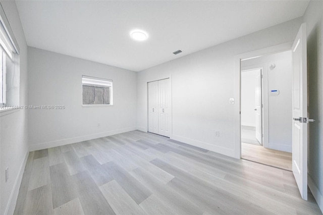 unfurnished bedroom featuring visible vents, baseboards, light wood finished floors, and a closet