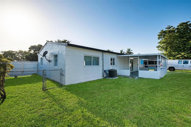 back of property with central AC, a sunroom, a yard, fence, and a gate