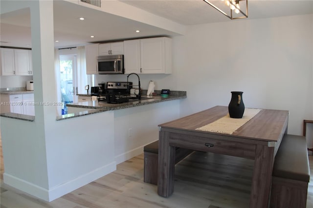 kitchen with dark stone countertops, white cabinets, appliances with stainless steel finishes, and light wood finished floors