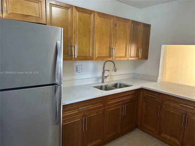 kitchen featuring brown cabinetry, light countertops, freestanding refrigerator, and a sink