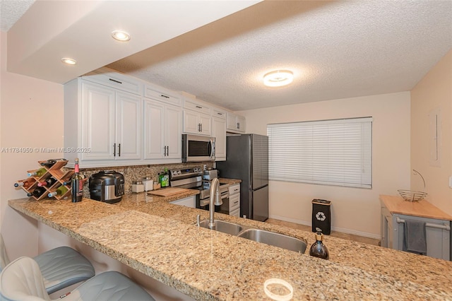kitchen featuring stainless steel appliances, a sink, a textured ceiling, backsplash, and white cabinetry