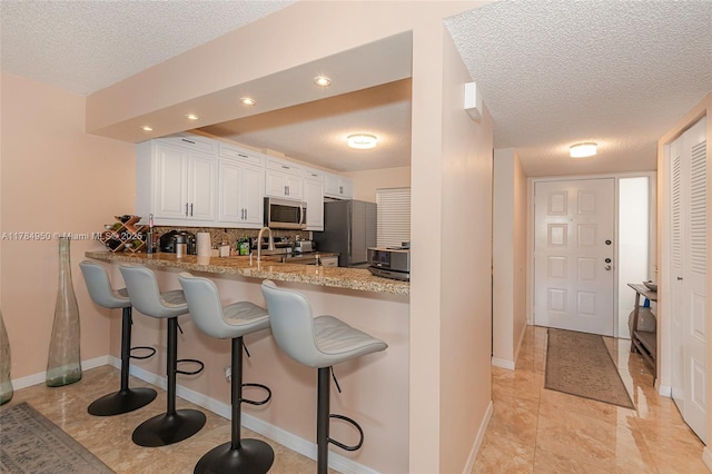 kitchen featuring a kitchen breakfast bar, a textured ceiling, white cabinets, a peninsula, and appliances with stainless steel finishes