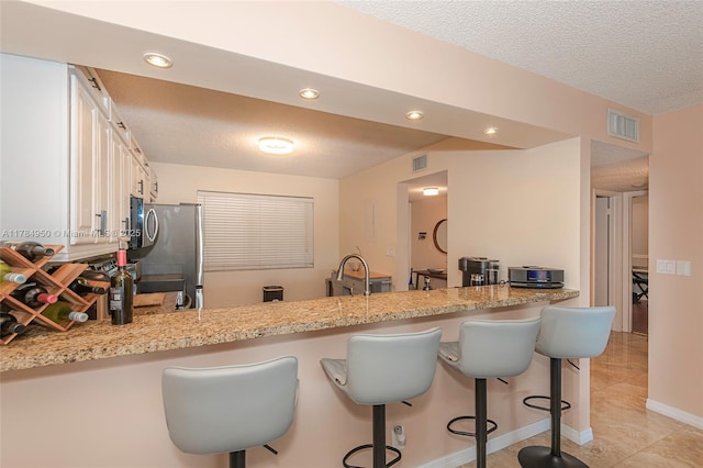 kitchen featuring white cabinets, a peninsula, a textured ceiling, freestanding refrigerator, and visible vents