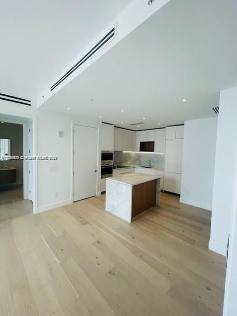 304 Ocean Dr Unit 302, Miami Beach, FL 33139 - kitchen featuring modern cabinets, white cabinetry, a kitchen island, light wood-type flooring, and stainless steel oven