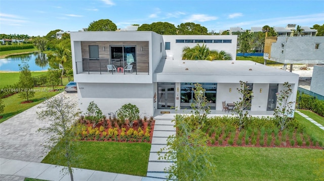 modern home featuring driveway, a balcony, a front lawn, a water view, and stucco siding