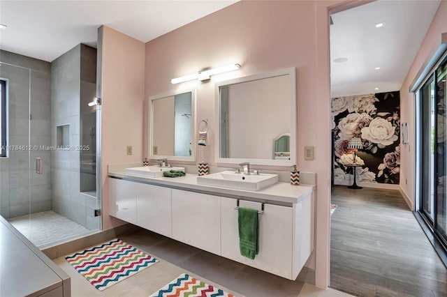 bathroom with wood finished floors, double vanity, a sink, and a stall shower
