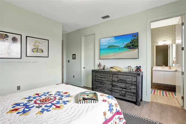 bedroom featuring ensuite bathroom, wood finished floors, and visible vents