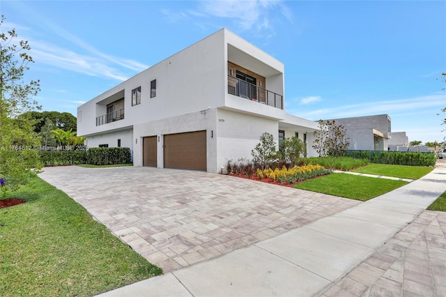 view of side of property featuring an attached garage, stucco siding, decorative driveway, a balcony, and a yard