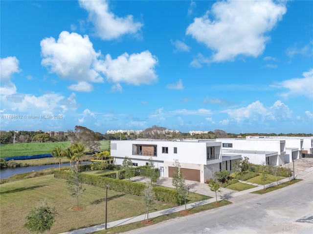 view of front of property with a garage, stucco siding, a front yard, a water view, and concrete driveway