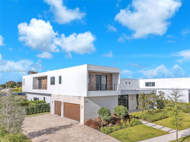 contemporary home with decorative driveway, an attached garage, a balcony, and stucco siding