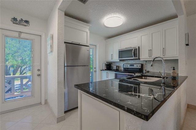 kitchen with dark stone countertops, a sink, appliances with stainless steel finishes, a textured ceiling, and white cabinetry