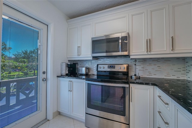 kitchen with light tile patterned floors, white cabinets, dark stone counters, stainless steel appliances, and backsplash