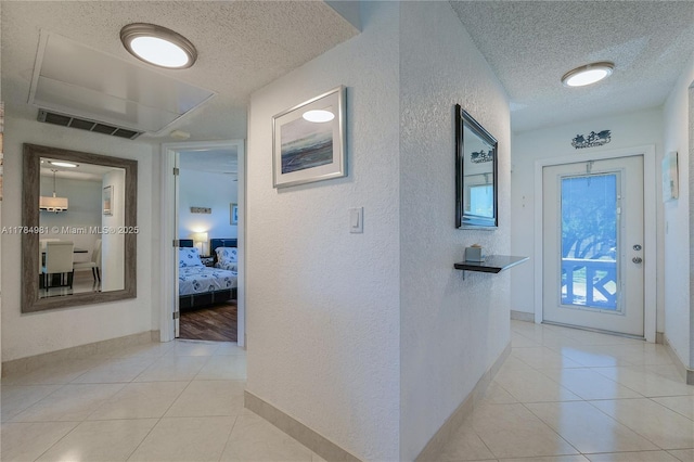 hallway featuring a textured ceiling, a textured wall, visible vents, and light tile patterned floors