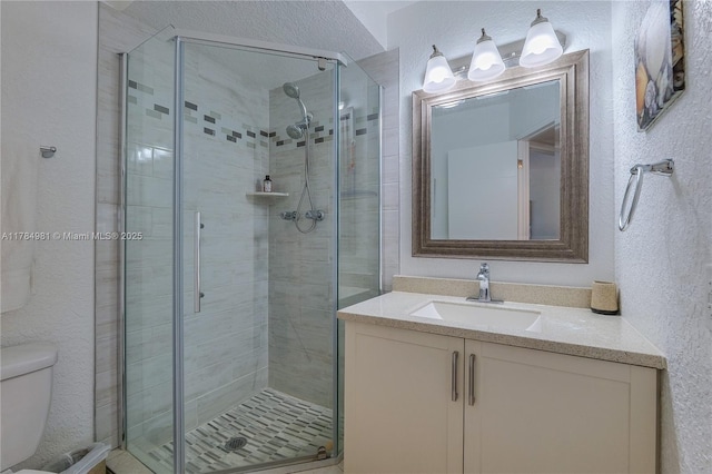 full bathroom featuring toilet, a shower stall, vanity, and a textured wall