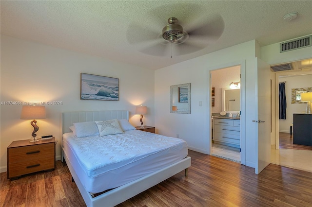 bedroom with a textured ceiling, wood finished floors, visible vents, and connected bathroom