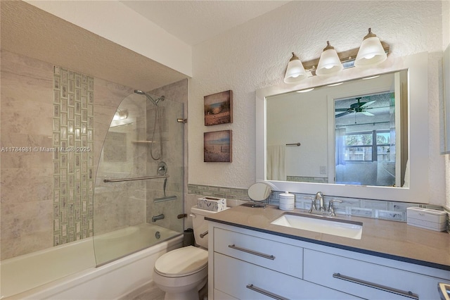 full bathroom featuring ceiling fan, vanity, toilet, bath / shower combo with glass door, and a textured wall