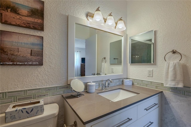 bathroom with tile walls, toilet, vanity, and a textured wall