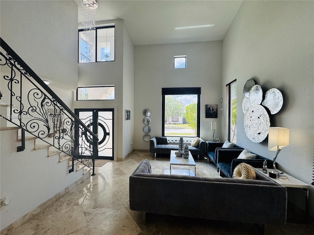 living area with a towering ceiling, stairway, a chandelier, marble finish floor, and baseboards