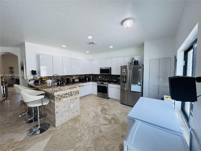 kitchen with a peninsula, white cabinetry, visible vents, appliances with stainless steel finishes, and arched walkways