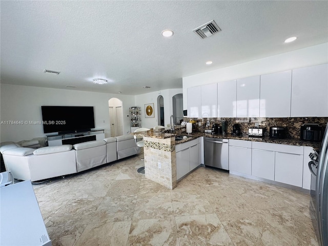 kitchen with visible vents, arched walkways, dishwasher, a sink, and a peninsula