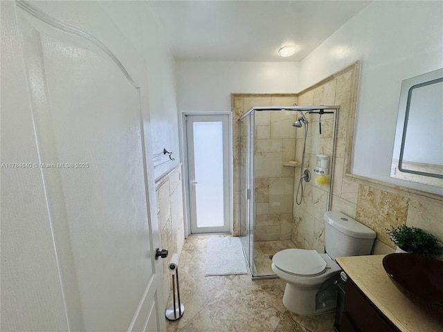 full bath with a shower stall, vanity, tile walls, and toilet