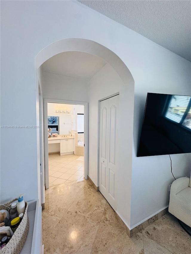 hall with baseboards, arched walkways, and a textured ceiling