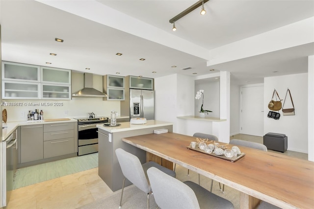 9250 W Bay Harbor Dr Unit 5C, Bay Harbor Islands, FL 33154 - kitchen with glass insert cabinets, wall chimney range hood, light countertops, appliances with stainless steel finishes, and gray cabinetry