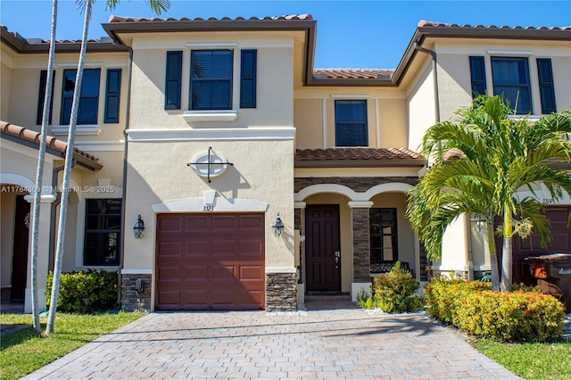 view of front of property with an attached garage, stone siding, a tile roof, stucco siding, and decorative driveway