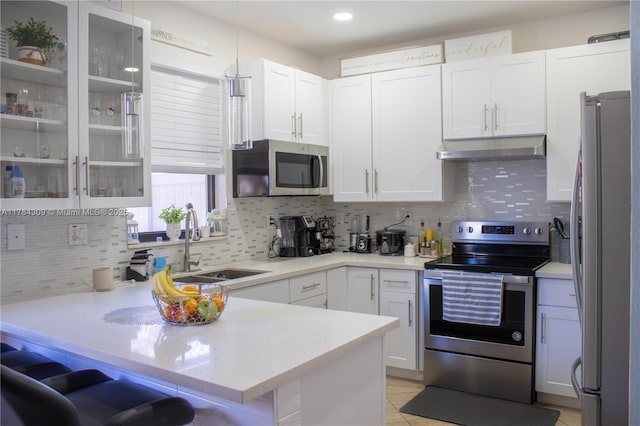 kitchen featuring a peninsula, white cabinets, under cabinet range hood, a sink, and stainless steel appliances