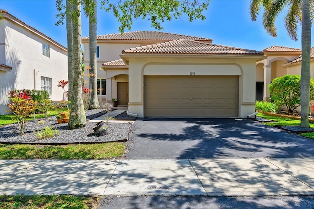 mediterranean / spanish house with an attached garage, a tiled roof, aphalt driveway, and stucco siding