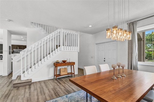dining area featuring wood finished floors, a notable chandelier, baseboards, and stairs