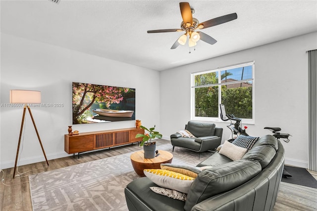 living area featuring a textured ceiling, wood finished floors, ceiling fan, and baseboards