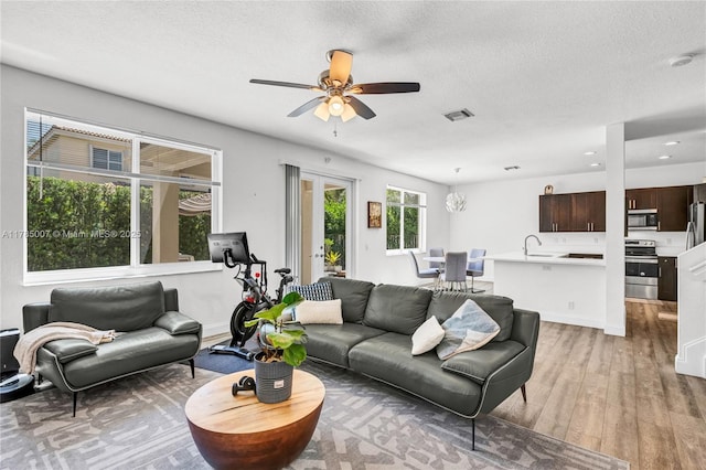 living area featuring light wood-style flooring, a textured ceiling, a ceiling fan, and visible vents