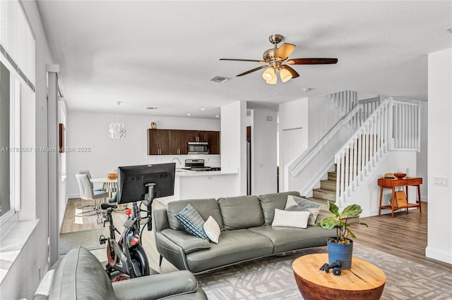 living room featuring light wood-type flooring, baseboards, stairs, visible vents, and ceiling fan