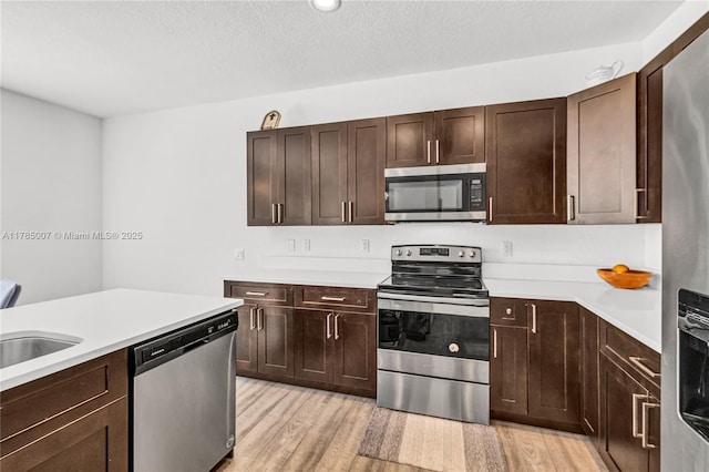 kitchen with dark brown cabinets, light countertops, appliances with stainless steel finishes, and light wood-style floors