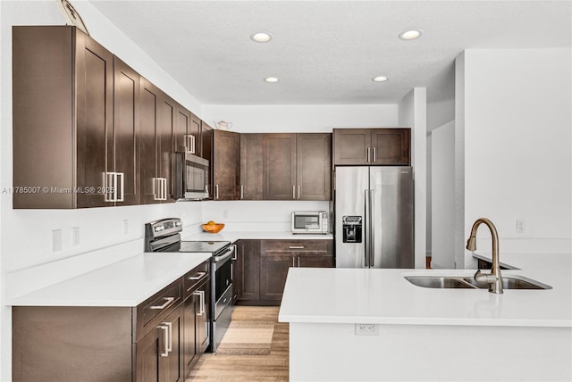 kitchen featuring dark brown cabinetry, recessed lighting, appliances with stainless steel finishes, light countertops, and a sink