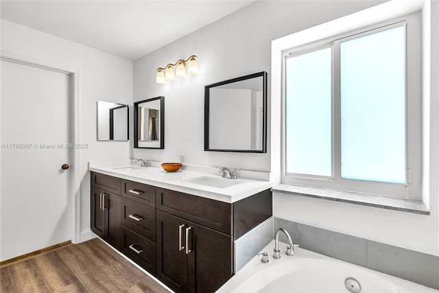 full bathroom with double vanity, a jetted tub, a sink, and wood finished floors