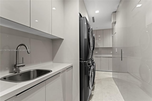 clothes washing area with stacked washing maching and dryer, light tile patterned floors, and a sink
